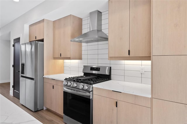 kitchen featuring light brown cabinetry, stainless steel appliances, light hardwood / wood-style flooring, and wall chimney exhaust hood