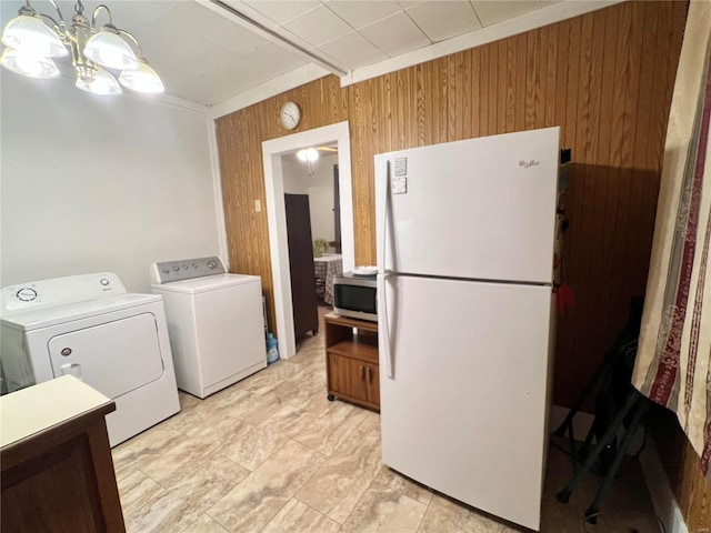 laundry area with an inviting chandelier, wooden walls, and washing machine and clothes dryer