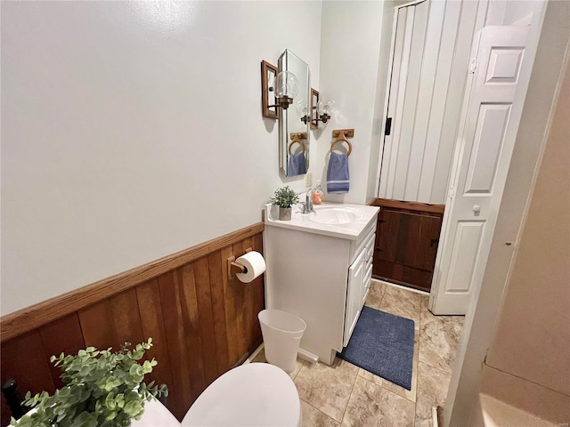 bathroom with vanity, toilet, and wood walls