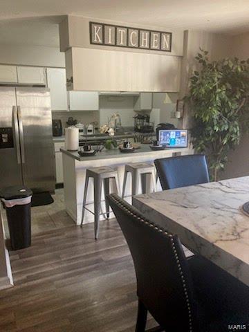 kitchen featuring a kitchen bar, stainless steel fridge, white cabinetry, and dark wood-type flooring