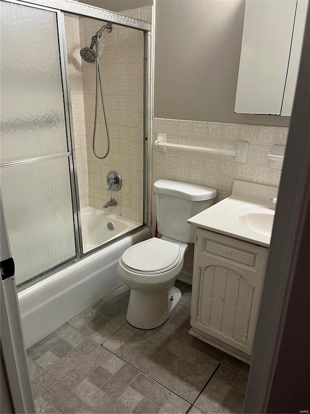 full bathroom featuring shower / bath combination with glass door, vanity, toilet, and tile walls