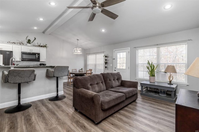 living room featuring ceiling fan, light hardwood / wood-style flooring, lofted ceiling with beams, and sink