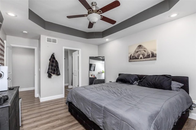 bedroom with hardwood / wood-style floors, ceiling fan, and a raised ceiling