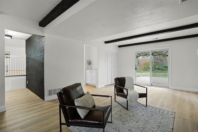 living room featuring beam ceiling, light hardwood / wood-style flooring, and brick wall