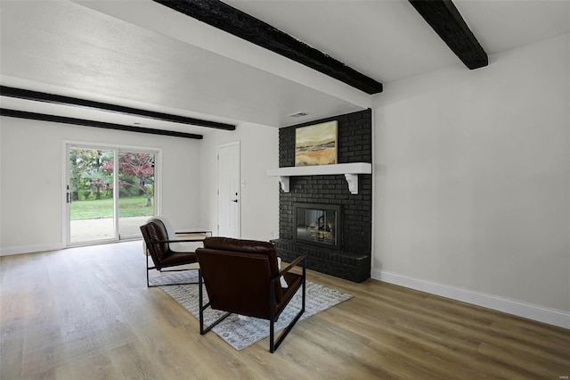 living room featuring beam ceiling, light hardwood / wood-style floors, and a brick fireplace