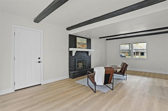 dining space with beamed ceiling, a brick fireplace, and light hardwood / wood-style flooring