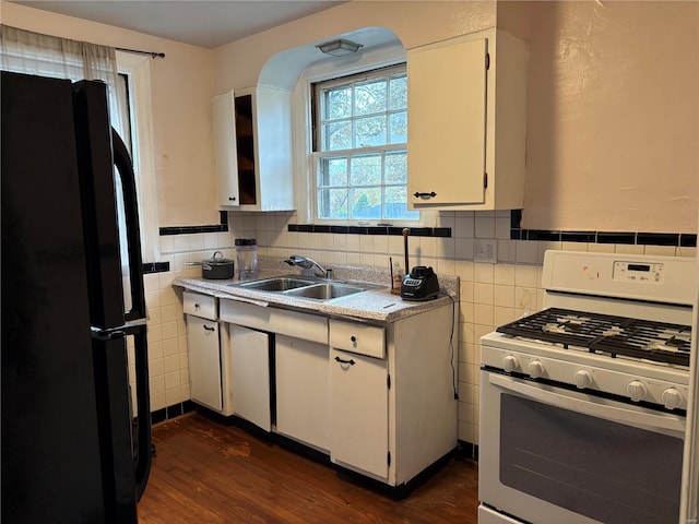 kitchen featuring black refrigerator, white gas range, dark wood-type flooring, sink, and white cabinets