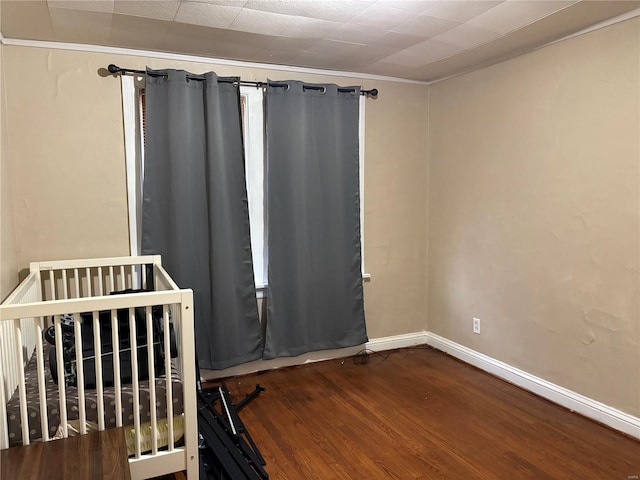 unfurnished bedroom with hardwood / wood-style flooring, a crib, and crown molding