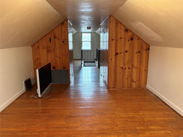 additional living space with hardwood / wood-style floors, wooden walls, and vaulted ceiling