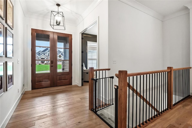 entryway with a notable chandelier, light wood-type flooring, crown molding, and french doors