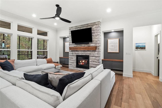 living room with ceiling fan, light hardwood / wood-style floors, a stone fireplace, and a healthy amount of sunlight