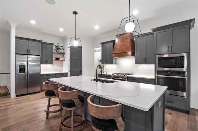 kitchen featuring a center island with sink, decorative light fixtures, premium range hood, and stainless steel appliances