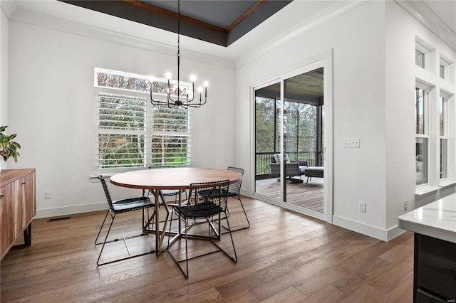 dining space featuring a tray ceiling, crown molding, an inviting chandelier, and hardwood / wood-style flooring