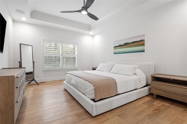 bedroom with light hardwood / wood-style floors, ceiling fan, and a tray ceiling