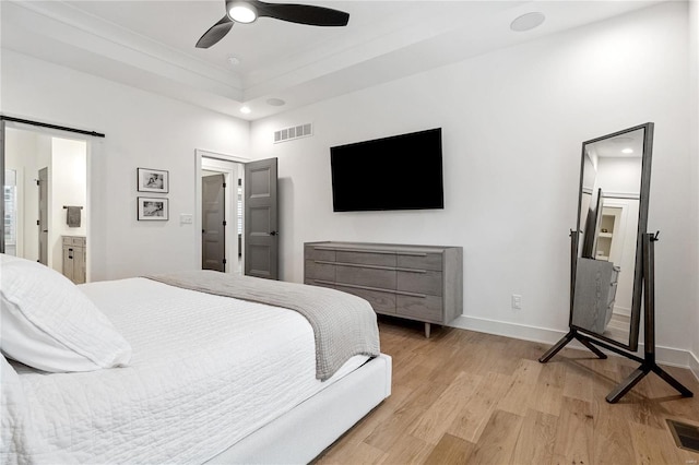 bedroom with ensuite bathroom, light hardwood / wood-style floors, a raised ceiling, and ceiling fan