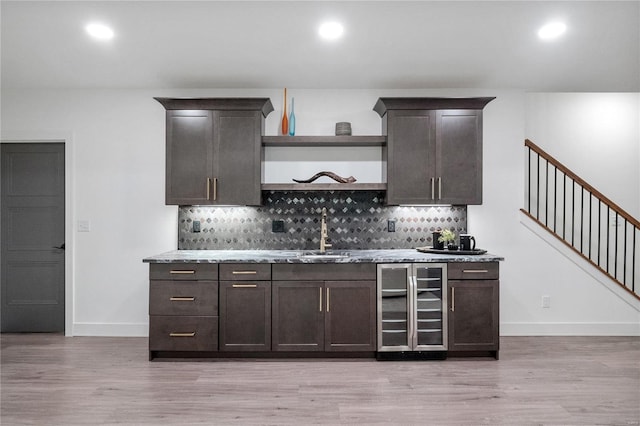 bar with dark brown cabinets, light hardwood / wood-style flooring, wine cooler, and sink