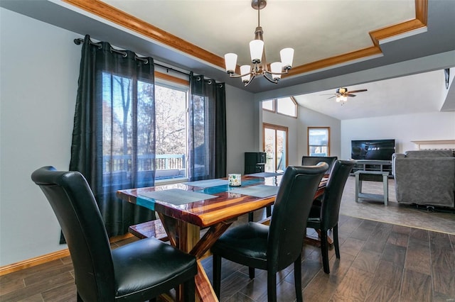 dining space with lofted ceiling, dark wood-type flooring, ceiling fan with notable chandelier, ornamental molding, and a tray ceiling