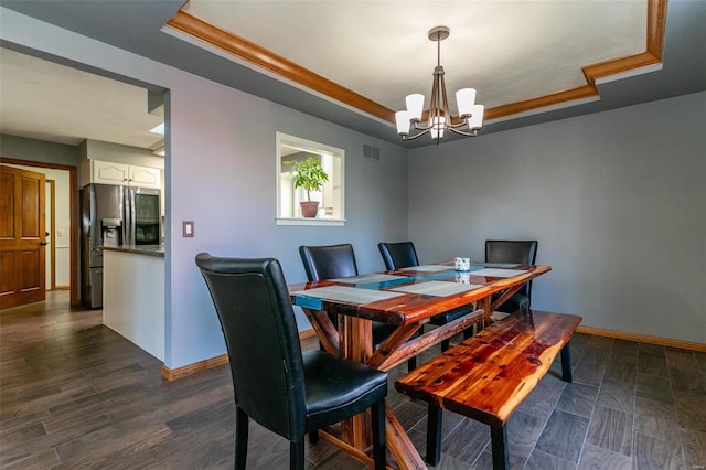 dining room with dark wood-type flooring, ornamental molding, a tray ceiling, and a notable chandelier