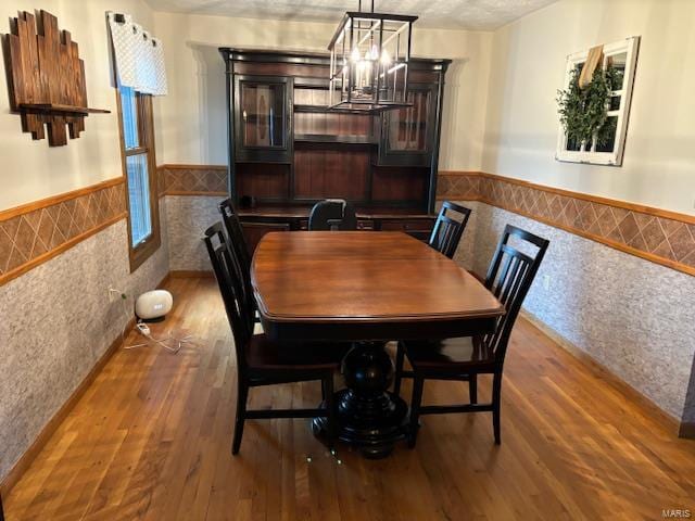 dining area with hardwood / wood-style floors, a notable chandelier, and tile walls