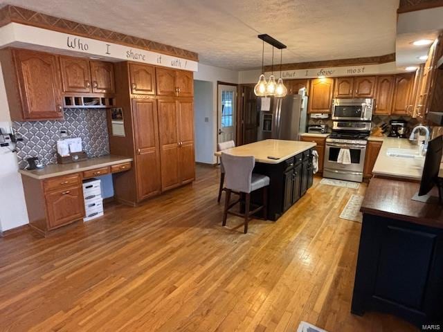 kitchen featuring sink, stainless steel appliances, backsplash, pendant lighting, and light wood-type flooring