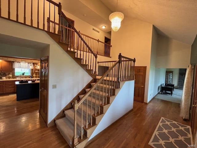 staircase with high vaulted ceiling, a notable chandelier, and hardwood / wood-style flooring