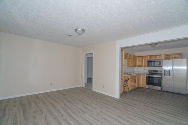 kitchen with appliances with stainless steel finishes, a textured ceiling, and light hardwood / wood-style floors