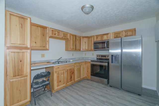 kitchen with appliances with stainless steel finishes, light brown cabinetry, a textured ceiling, sink, and light hardwood / wood-style floors