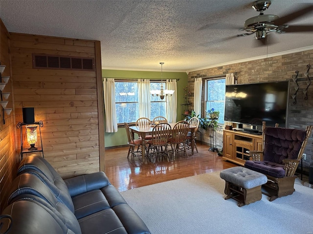 living room featuring ceiling fan with notable chandelier, hardwood / wood-style flooring, ornamental molding, and wood walls