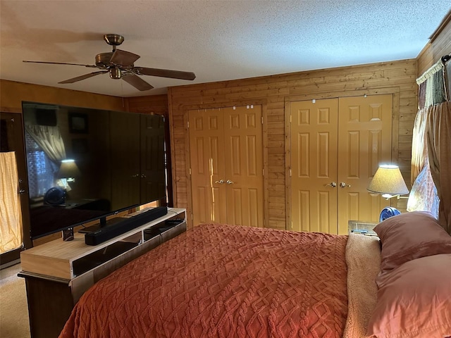 bedroom featuring carpet, a textured ceiling, ceiling fan, wooden walls, and multiple closets