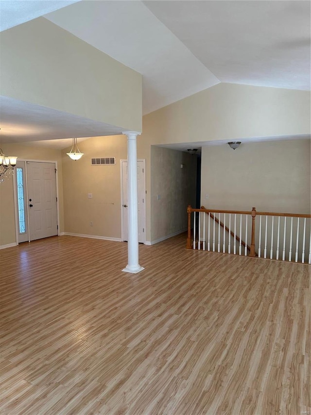 spare room featuring light wood-type flooring, visible vents, vaulted ceiling, and ornate columns