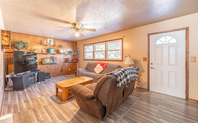 living room featuring hardwood / wood-style floors, ceiling fan, a textured ceiling, and wooden walls