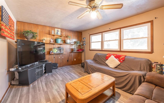 living room with a textured ceiling, light hardwood / wood-style floors, ceiling fan, and wood walls