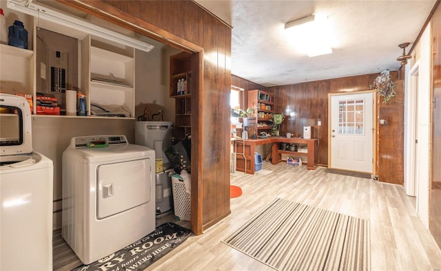 washroom with light hardwood / wood-style floors, wood walls, washing machine and dryer, and electric water heater