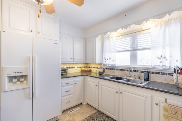 kitchen with white refrigerator with ice dispenser, dark countertops, a sink, and visible vents