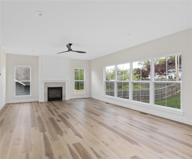 unfurnished living room with ceiling fan, a healthy amount of sunlight, light hardwood / wood-style floors, and a tile fireplace