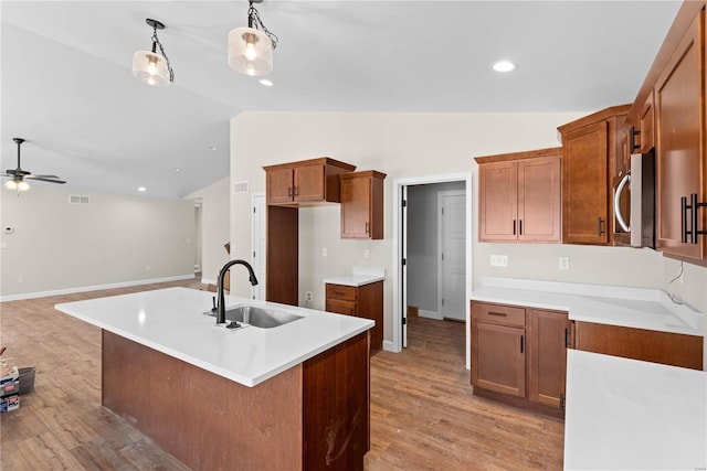 kitchen featuring sink, ceiling fan, light wood-type flooring, hanging light fixtures, and a center island with sink