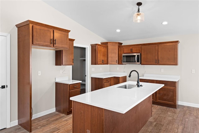 kitchen with sink, decorative light fixtures, vaulted ceiling, an island with sink, and wood-type flooring