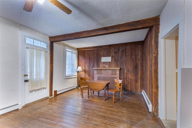 dining area with beam ceiling, ceiling fan, a baseboard heating unit, and wood walls