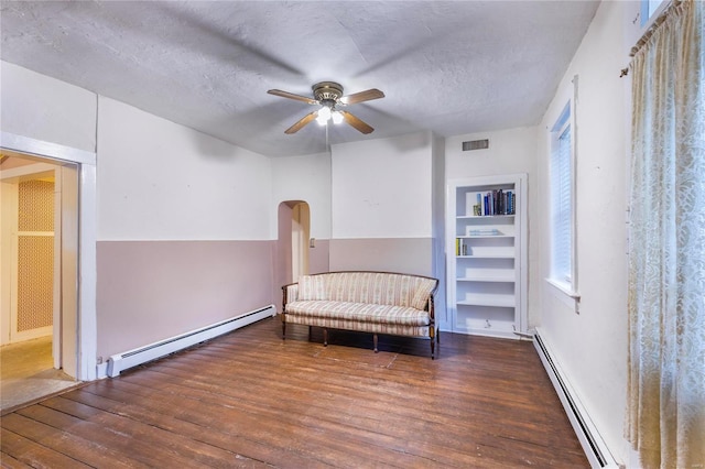 living area featuring built in shelves, a textured ceiling, baseboard heating, and ceiling fan