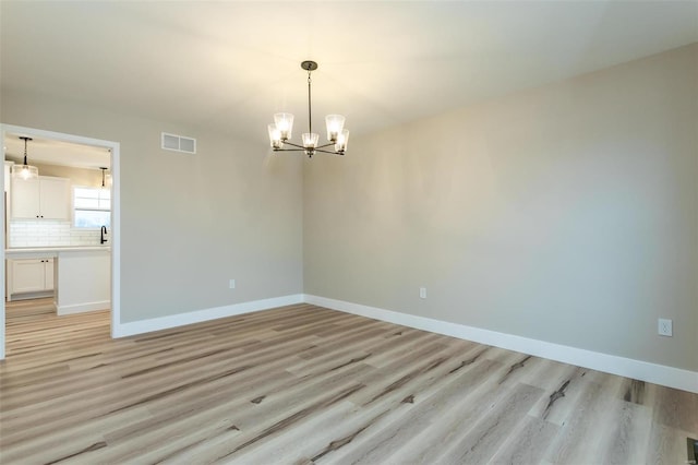 empty room with sink, a chandelier, and light hardwood / wood-style floors