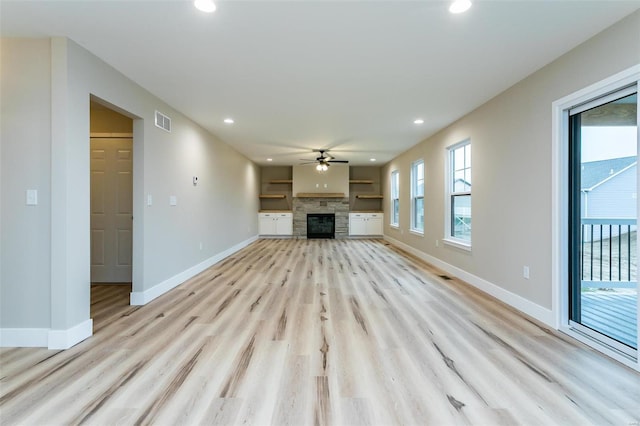 unfurnished living room featuring ceiling fan, a stone fireplace, and light hardwood / wood-style flooring