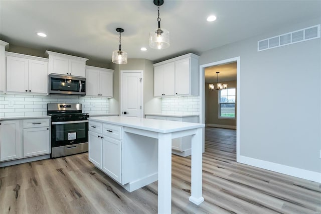 kitchen with white cabinetry, pendant lighting, stainless steel appliances, and light hardwood / wood-style floors