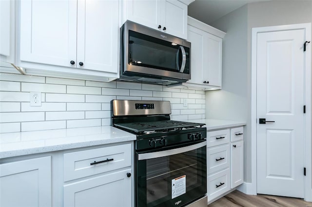 kitchen featuring tasteful backsplash, white cabinetry, light stone counters, stainless steel appliances, and light wood-type flooring