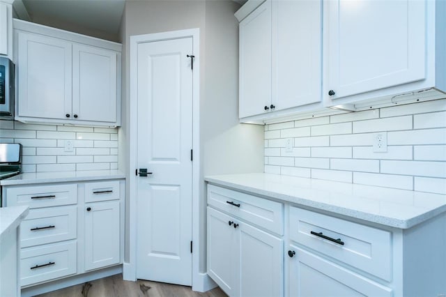 kitchen with light stone countertops, white cabinets, light wood-type flooring, and decorative backsplash