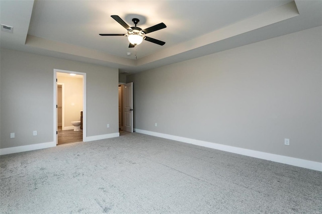 unfurnished bedroom with ceiling fan, carpet flooring, ensuite bathroom, and a tray ceiling