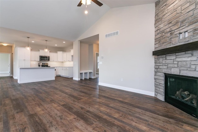 unfurnished living room featuring ceiling fan, a fireplace, dark hardwood / wood-style floors, and high vaulted ceiling