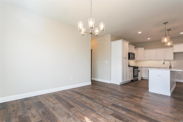 kitchen featuring appliances with stainless steel finishes, dark hardwood / wood-style floors, pendant lighting, white cabinetry, and a kitchen island with sink