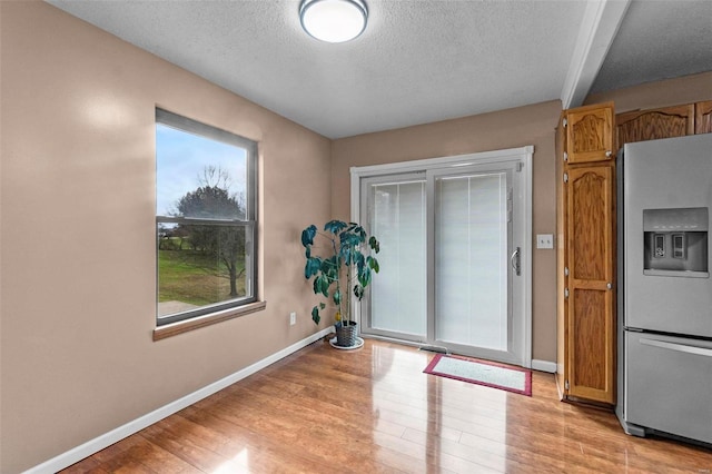 entryway with beam ceiling, light hardwood / wood-style floors, and a textured ceiling