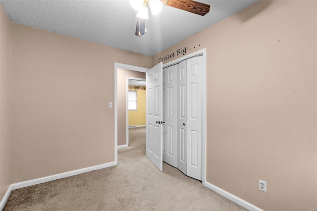 unfurnished bedroom with ceiling fan, a closet, light carpet, and a textured ceiling