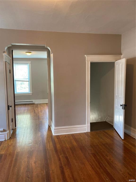 empty room with dark hardwood / wood-style flooring and a baseboard heating unit